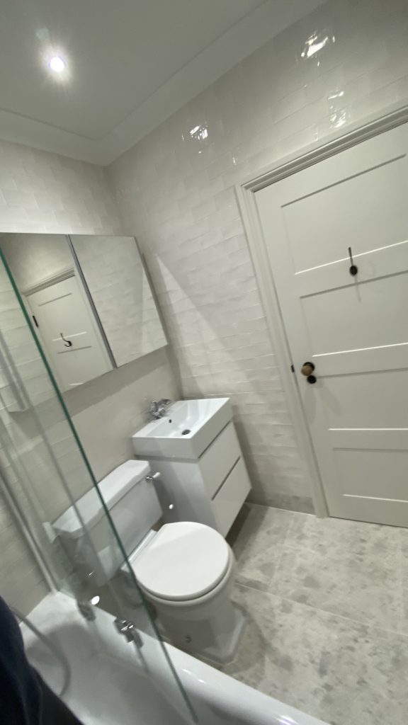 Modern bathroom interior with white tiles, compact sink unit, and white door, showcasing expert renovation work in Wandsworth and South London.