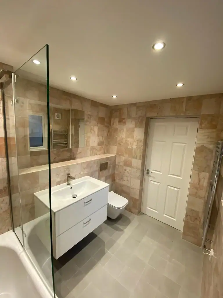 Inviting Dulwich bathroom with beige terracotta wall tiles, white bathtub with glass shower screen, floating white vanity, back-to-wall white toilet, gray porcelain floor tiles, and recessed ceiling lights
