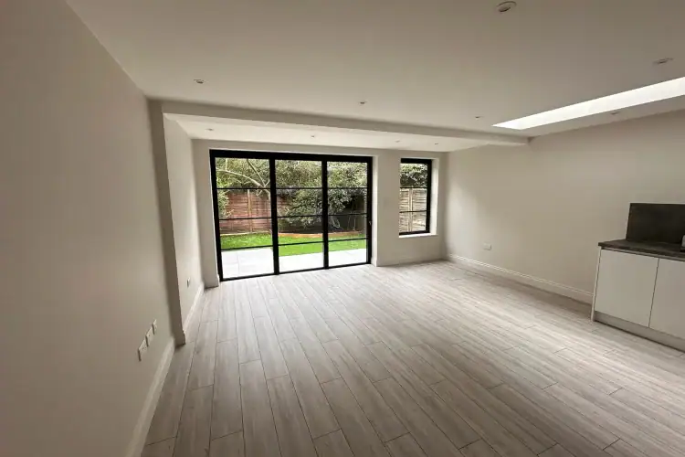 Overhead linear rooflight with frosted glazing, multiple recessed downlights casting even glow on white cabinets and oak floors in a Balham home extension