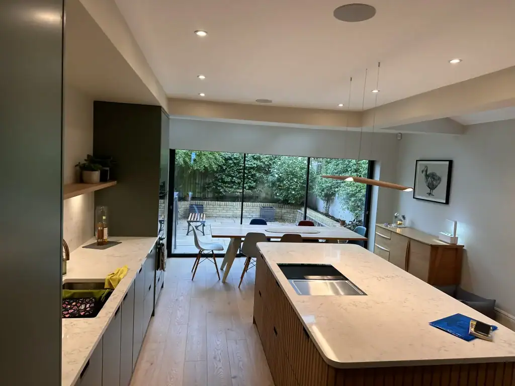 Close-up of sleek white marble island with induction hob, downdraft extractor, sage green base cabinets, pendant lighting, and herb pots in a renovated Clapham luxury kitchen