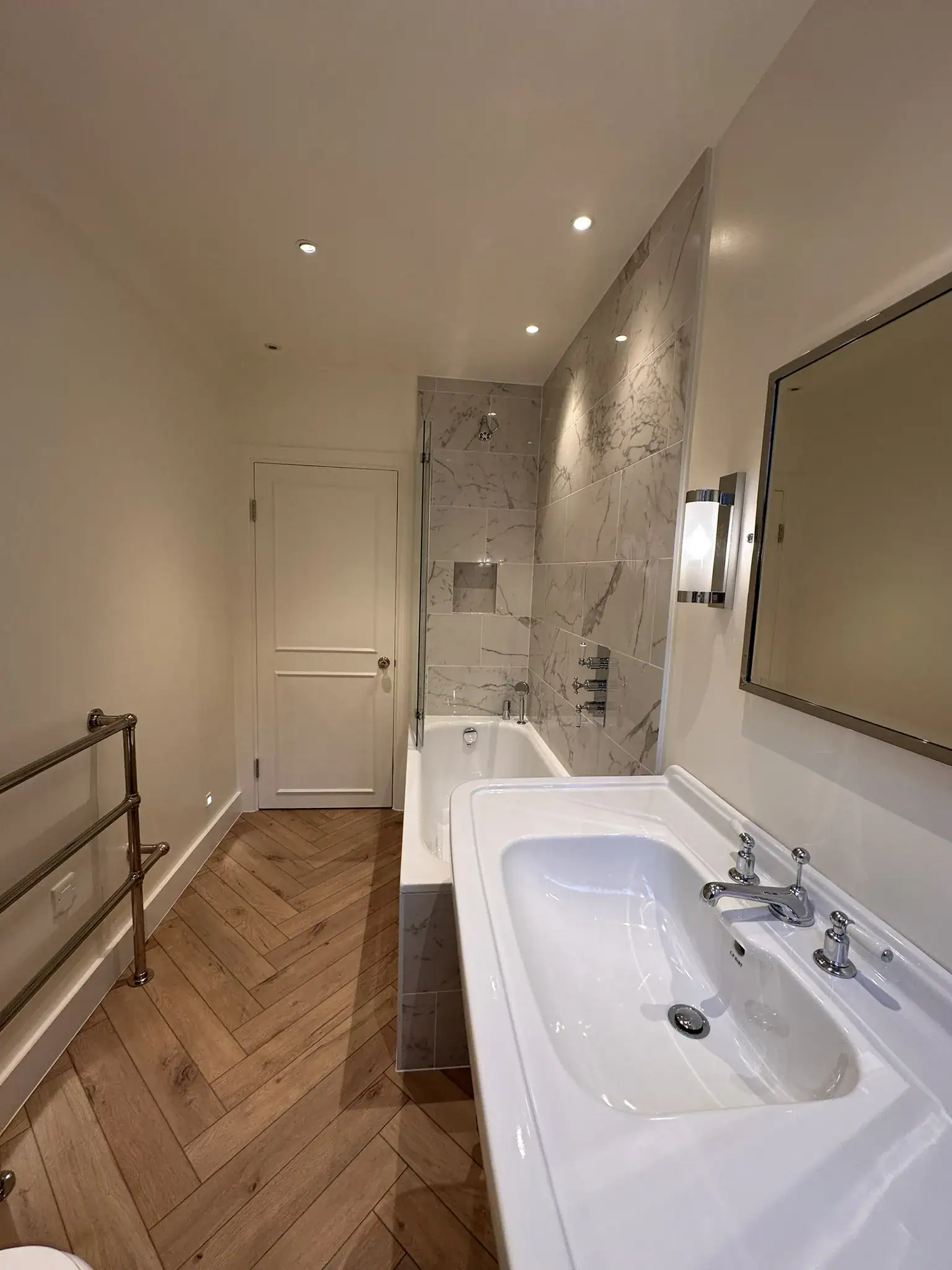Detailed view of glossy white marble wall tiles, frameless glass shower screen, thermostatic mixer taps, and integrated niche in a renovated South Kensington bathroom.