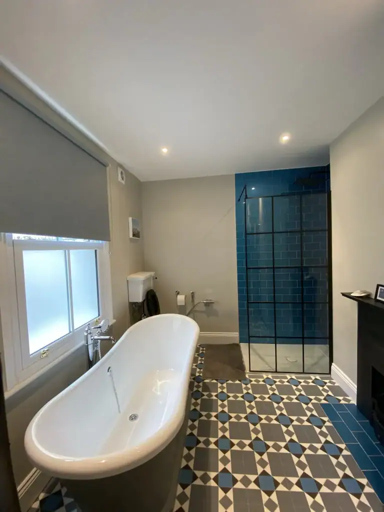 Close-up of frameless black steel shower enclosure with glossy blue porcelain tiles, overhead rainfall head, and integrated niche shelving in a renovated Dulwich bathroom.