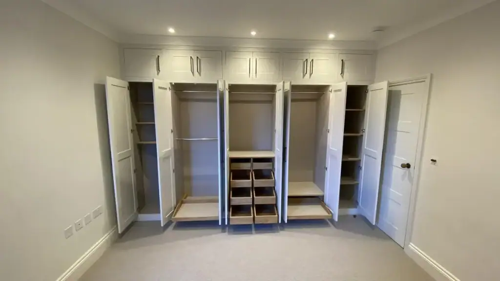 Open double wardrobe doors revealing oak shelving, hanging rails, and drawers in neutral-toned fitted cabinetry for contemporary bedroom